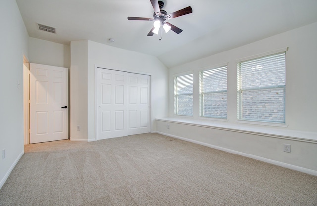 unfurnished bedroom featuring visible vents, baseboards, light colored carpet, vaulted ceiling, and a closet