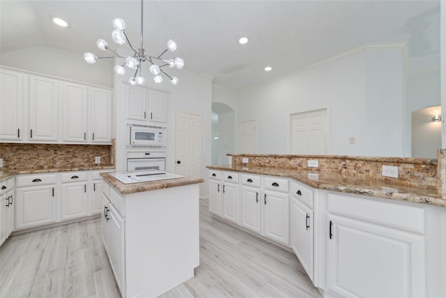 kitchen featuring arched walkways, white appliances, white cabinetry, and backsplash