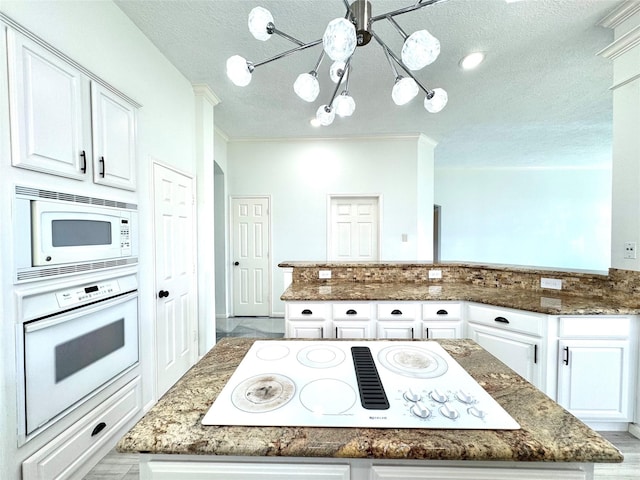 kitchen featuring a notable chandelier, a peninsula, white appliances, white cabinets, and dark stone counters