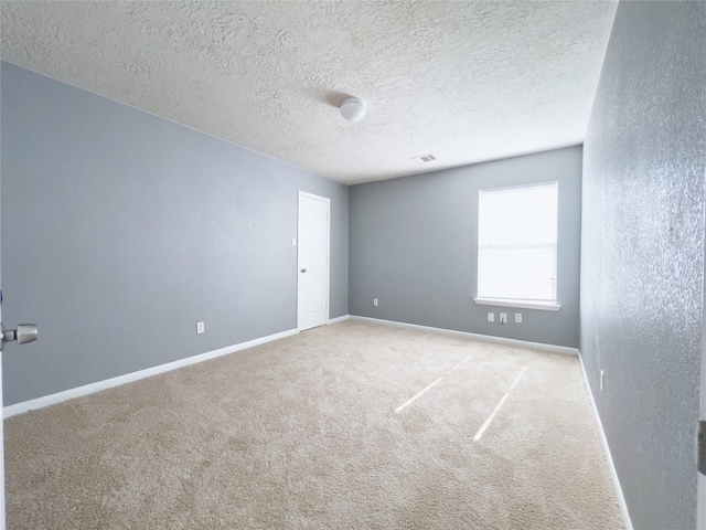 empty room featuring visible vents, baseboards, carpet flooring, and a textured wall