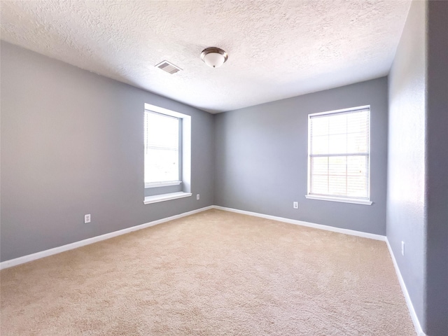 spare room featuring baseboards, visible vents, a textured ceiling, and light colored carpet