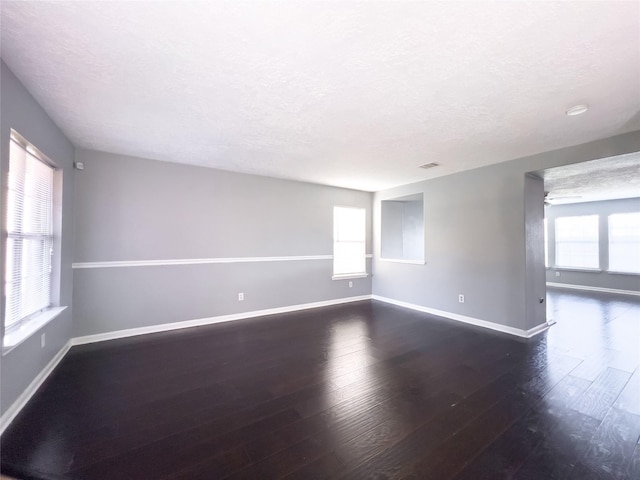 empty room featuring a textured ceiling, wood finished floors, and baseboards