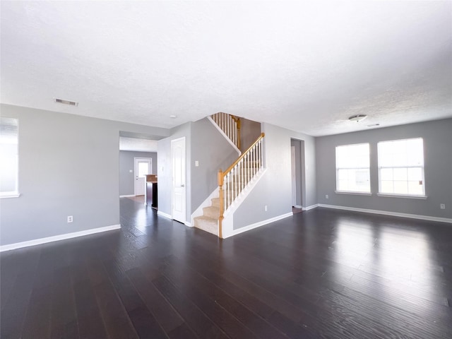 unfurnished room with a textured ceiling, wood finished floors, visible vents, baseboards, and stairway