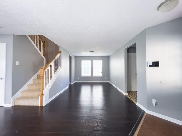 spare room with stairs, a textured ceiling, wood finished floors, and baseboards