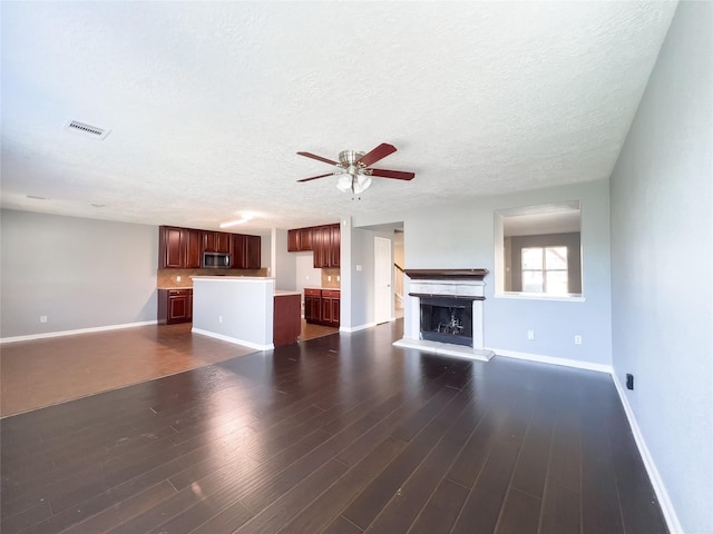 unfurnished living room featuring visible vents, a fireplace with raised hearth, dark wood-type flooring, a textured ceiling, and baseboards