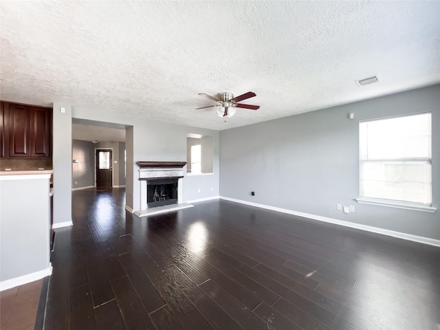 unfurnished living room with a fireplace with raised hearth, dark wood-style floors, visible vents, and a healthy amount of sunlight