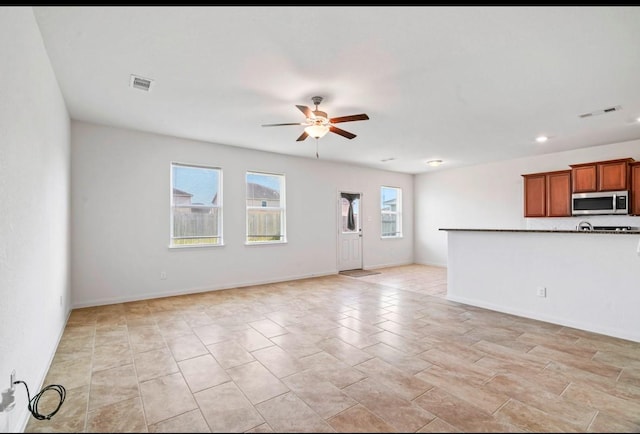 unfurnished living room featuring baseboards, visible vents, and a ceiling fan