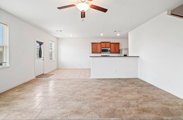 unfurnished living room featuring ceiling fan, light tile patterned floors, baseboards, and a healthy amount of sunlight