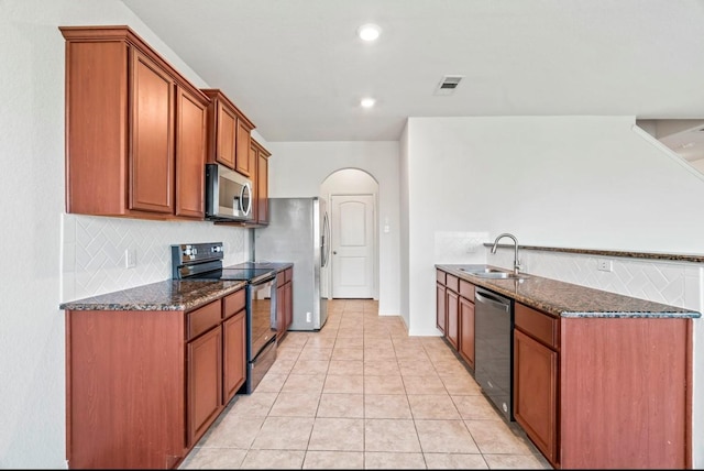 kitchen with arched walkways, stainless steel appliances, a sink, visible vents, and dark stone countertops