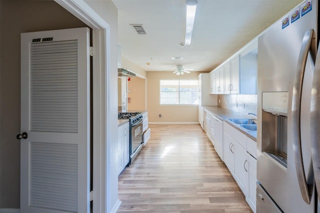 kitchen with a sink, visible vents, white cabinets, range with gas cooktop, and stainless steel fridge