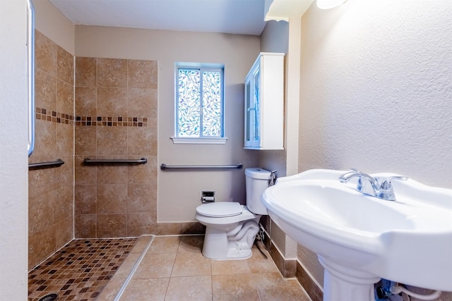 bathroom featuring toilet, a sink, a tile shower, baseboards, and tile patterned floors