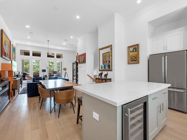 kitchen with wine cooler, light wood-style flooring, white cabinets, ornamental molding, and freestanding refrigerator