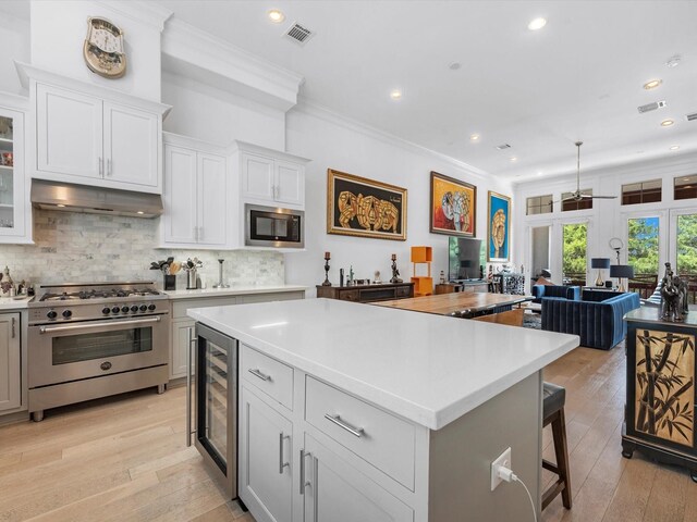 kitchen with light countertops, stainless steel appliances, a center island, under cabinet range hood, and visible vents