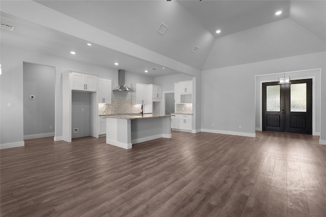 kitchen featuring dark wood finished floors, decorative backsplash, white cabinets, an island with sink, and wall chimney exhaust hood