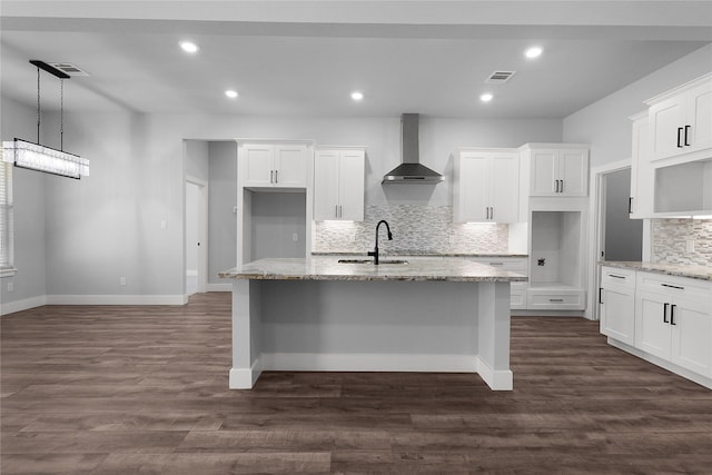 kitchen featuring visible vents, wall chimney range hood, a sink, and a center island with sink