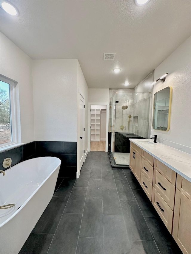 full bathroom featuring a walk in closet, visible vents, a freestanding bath, a shower stall, and vanity