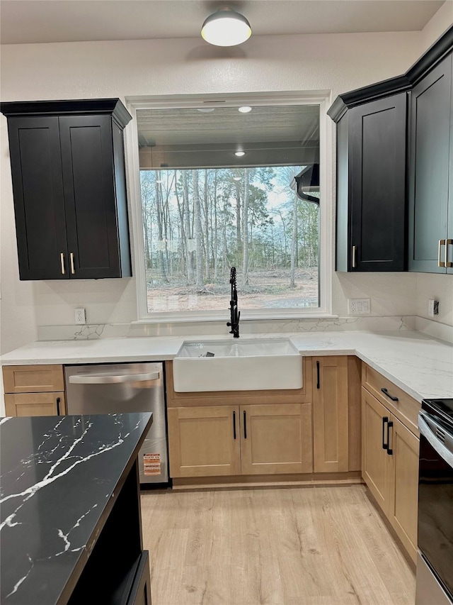 kitchen featuring light wood-type flooring, light stone countertops, appliances with stainless steel finishes, and a sink