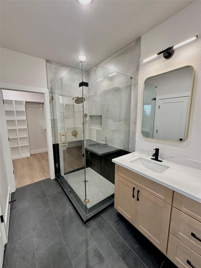 full bathroom featuring a walk in closet, a stall shower, vanity, a textured ceiling, and tile patterned flooring