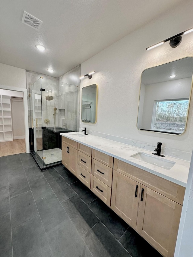 bathroom with a stall shower, visible vents, a sink, and double vanity