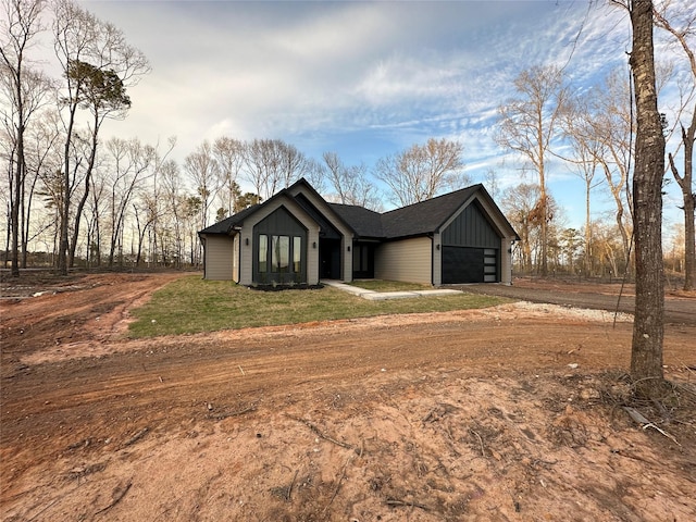 view of front of property with board and batten siding, a garage, a front lawn, and dirt driveway