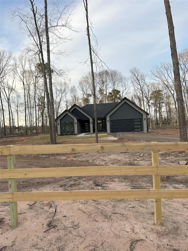 view of front of house featuring driveway, board and batten siding, an attached garage, and fence