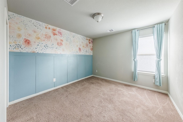 spare room with wallpapered walls, carpet, visible vents, and wainscoting