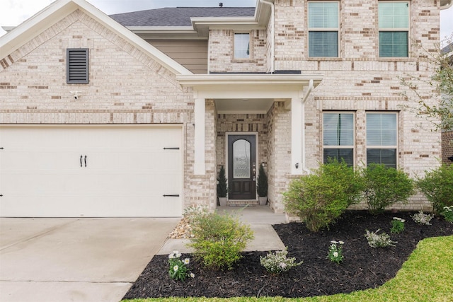 doorway to property featuring a garage, brick siding, driveway, and a shingled roof