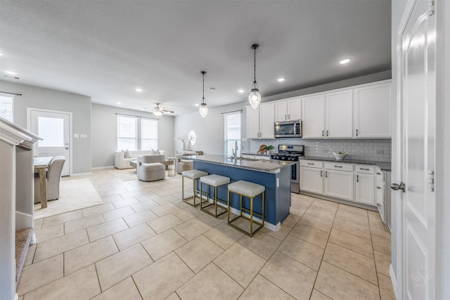 kitchen featuring stainless steel appliances, decorative backsplash, open floor plan, light tile patterned flooring, and a sink