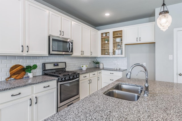 kitchen featuring appliances with stainless steel finishes, white cabinetry, a sink, and glass insert cabinets