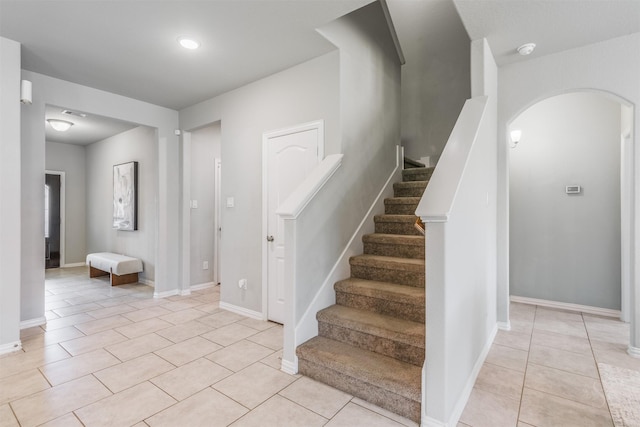 stairway with arched walkways, tile patterned flooring, and baseboards