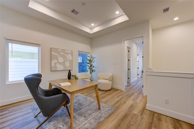 home office with light wood-type flooring, baseboards, visible vents, and a tray ceiling