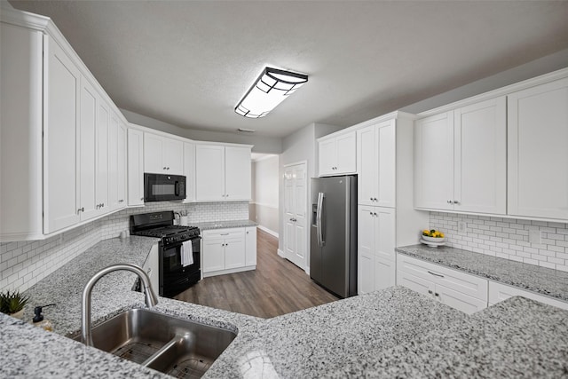 kitchen with black appliances, light stone counters, a sink, and white cabinetry