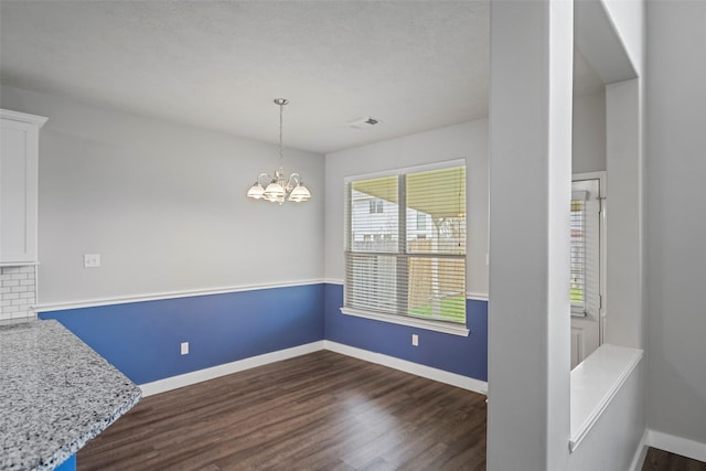 unfurnished dining area featuring dark wood-style floors, visible vents, baseboards, and an inviting chandelier