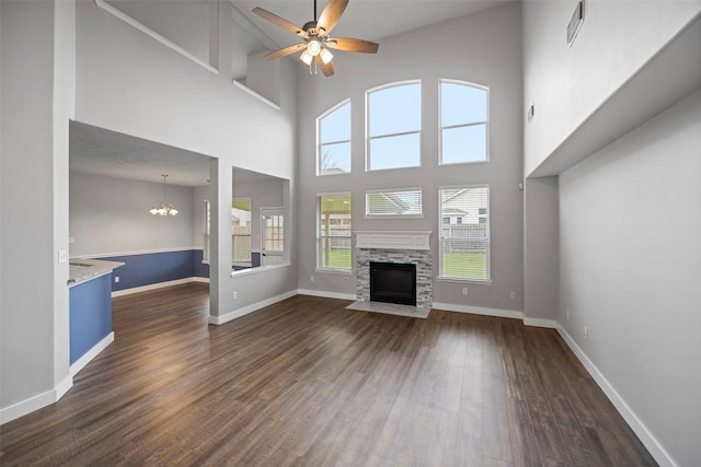 unfurnished living room with dark wood finished floors, visible vents, a stone fireplace, baseboards, and ceiling fan with notable chandelier