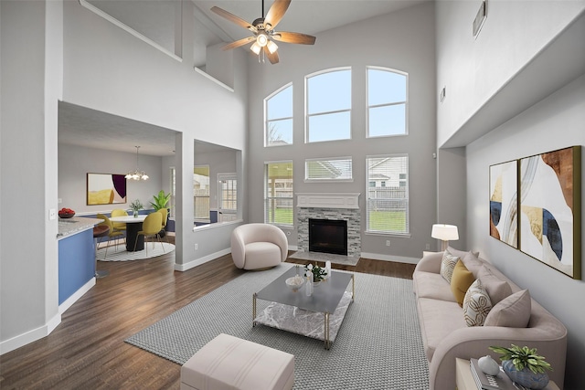 living area featuring ceiling fan with notable chandelier, a fireplace, visible vents, baseboards, and dark wood-style floors