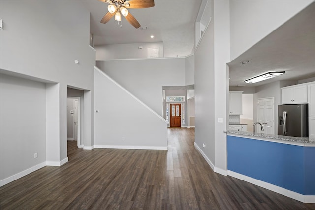 unfurnished living room featuring dark wood-type flooring, baseboards, and a ceiling fan