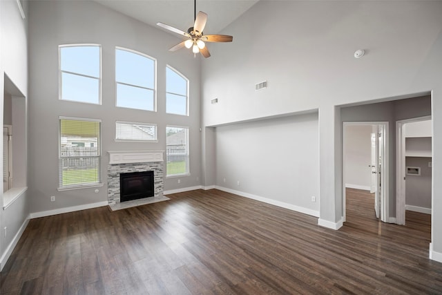 unfurnished living room featuring dark wood-style floors, ceiling fan, baseboards, and a stone fireplace