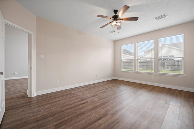 empty room with dark wood-style floors, baseboards, visible vents, and ceiling fan