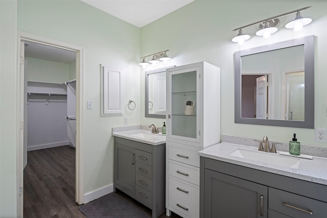 bathroom featuring two vanities, a sink, a spacious closet, and baseboards