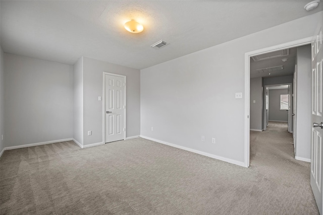 empty room with visible vents, carpet floors, attic access, and baseboards