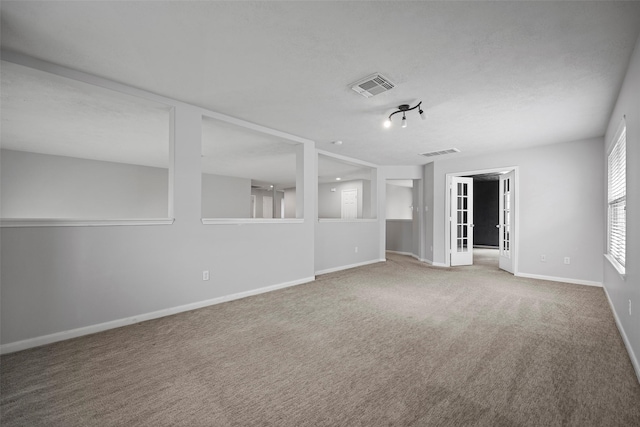 carpeted empty room with a textured ceiling, visible vents, and baseboards