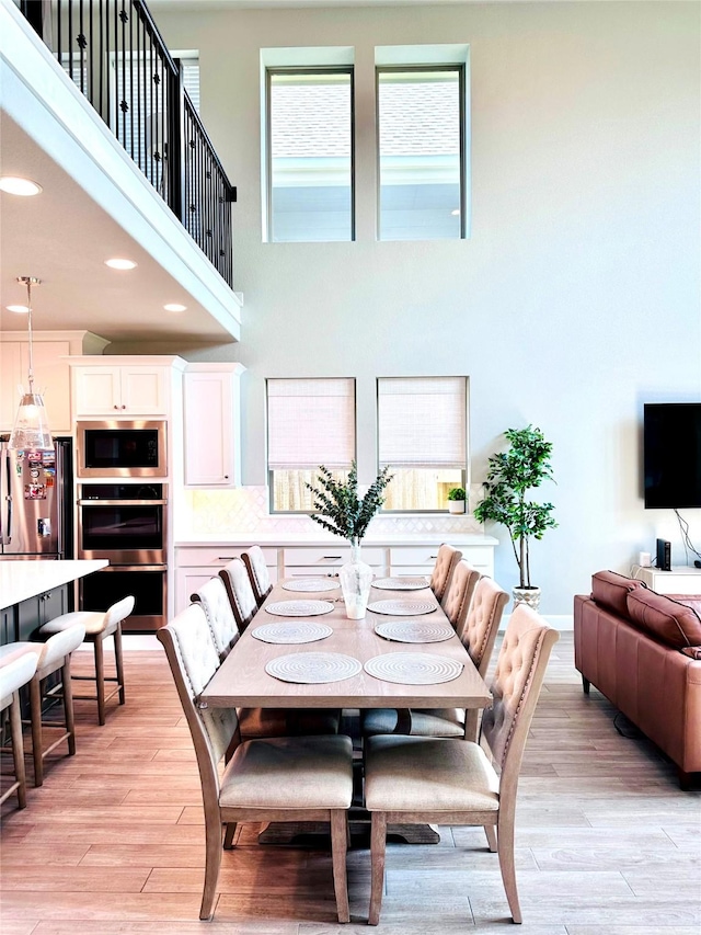 dining room with recessed lighting, a high ceiling, and light wood-style flooring