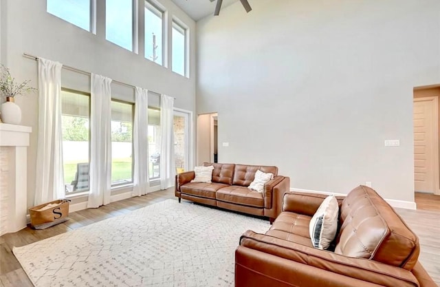 living area with light wood-style flooring, a towering ceiling, and ceiling fan