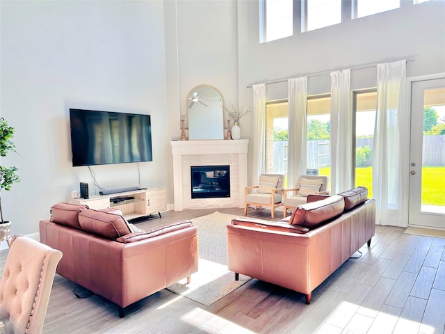 living room featuring ceiling fan, light wood-type flooring, a towering ceiling, and a tiled fireplace