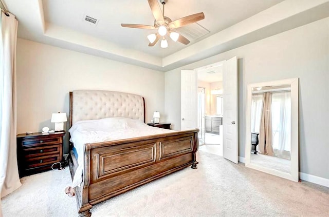 bedroom with visible vents, baseboards, light colored carpet, ensuite bath, and a raised ceiling