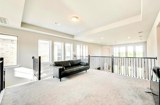 living area with visible vents, carpet, and a tray ceiling