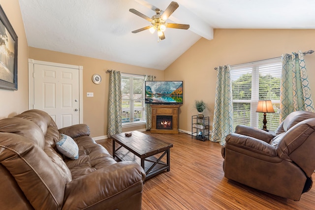 living room featuring a warm lit fireplace, lofted ceiling with beams, wood finished floors, and a healthy amount of sunlight