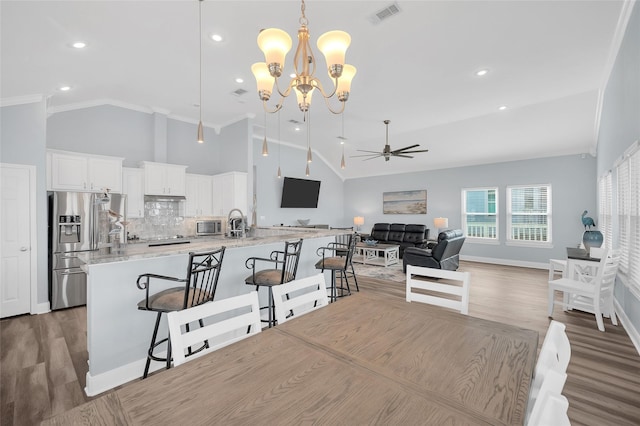 kitchen with visible vents, ornamental molding, stainless steel fridge, a kitchen bar, and ceiling fan with notable chandelier