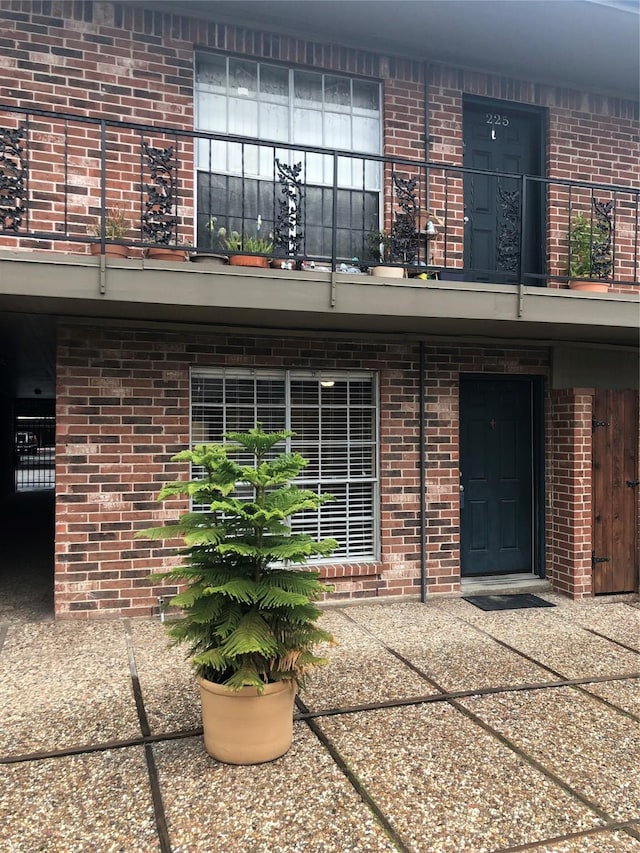 view of exterior entry featuring brick siding and a balcony