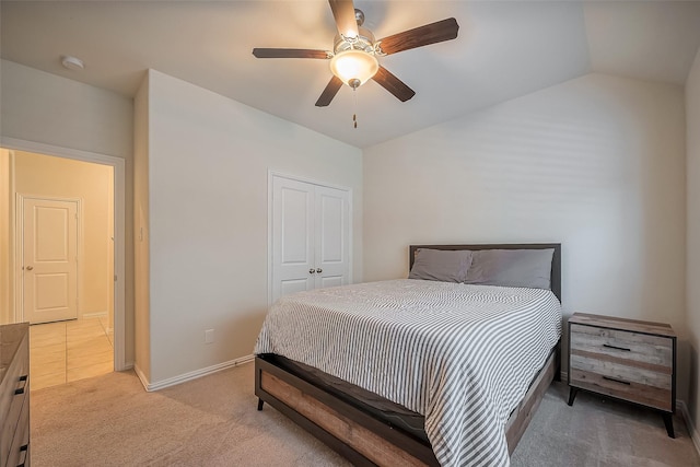 bedroom with lofted ceiling, light carpet, a ceiling fan, baseboards, and a closet